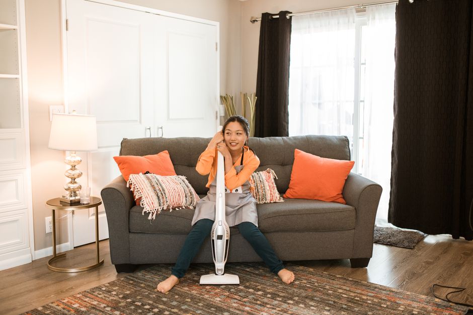 Woman in apron sitting on couch with vacuum cleaner in stylish living room.