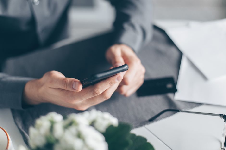 A close-up view of a man's hands using a smartphone with papers on a table.